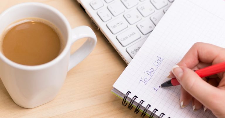 Person writing "To Do List" on a notepad with coffee and keyboard nearby.