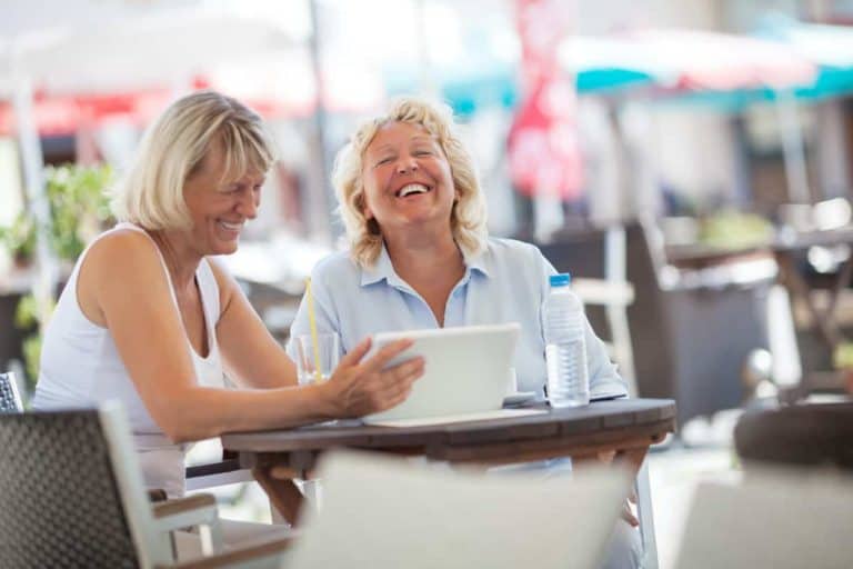 Two women enjoying humor and memes outdoors at a cafe.