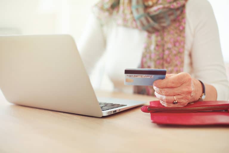 Senior woman's hand holding a credit card while in front of the laptop shopping online